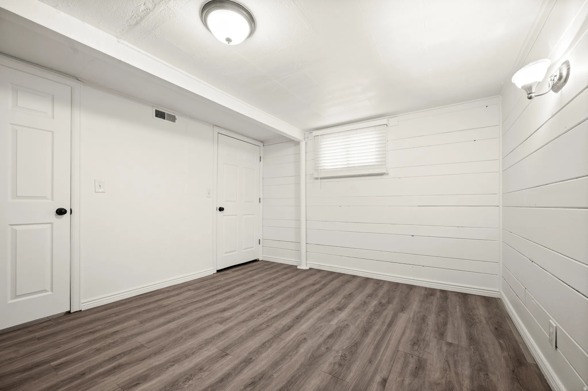 Wood-finish flooring, white paneled doors, recessed ceiling light, wall-mounted sconce, and white window blinds