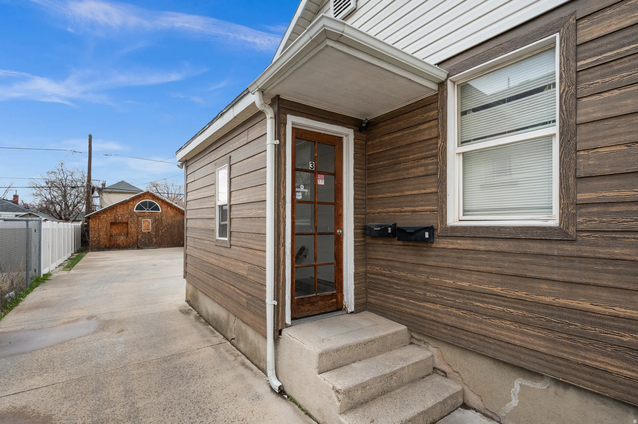 Exterior with horizontal wood-finish siding, white trim windows, and a concrete pathway leading to a glass-paneled entry door