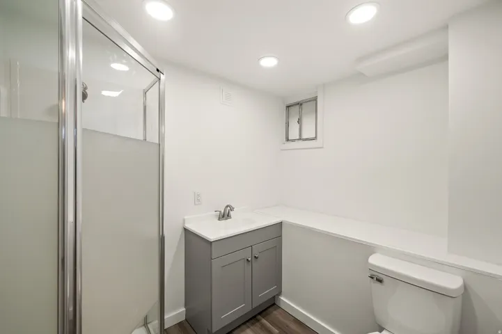 Shower with framed frosted glass enclosure, gray vanity with integrated sink, wood-finish flooring, and recessed lighting