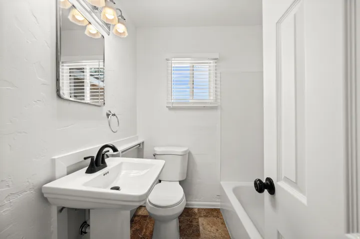 Pedestal sink with black-finish faucet, wall-mounted mirror, and vanity lighting