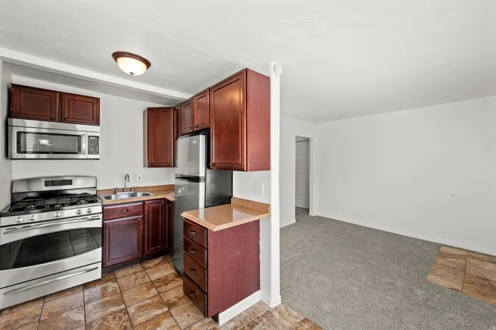 Kitchen featuring wood cabinetry, stainless steel appliances, a double basin sink, and a light-toned countertop