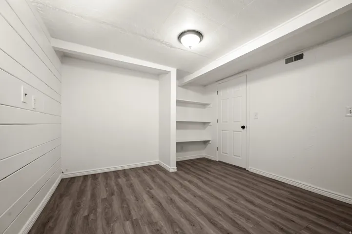 Wood-finish flooring, built-in shelving, white paneled walls, and a ceiling-mounted light fixture