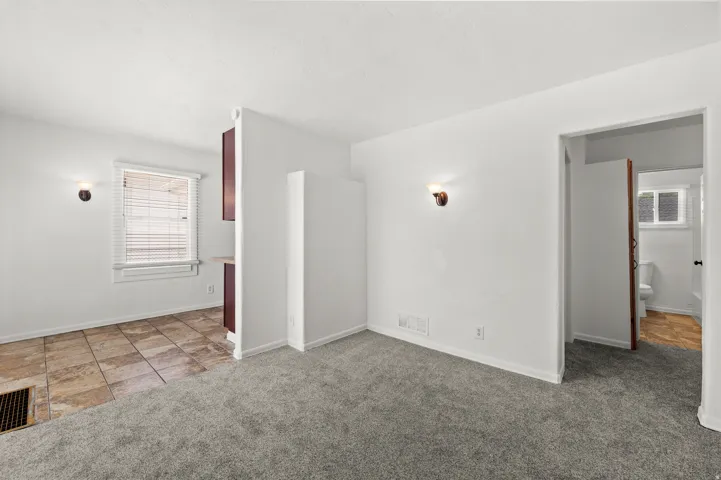 Neutral wall color with wall-mounted sconces, plush grey carpeting, and a tiled floor area