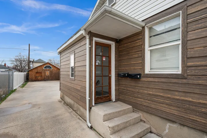 Exterior with horizontal wood-finish siding, white trim windows, and a concrete pathway leading to a glass-paneled entry door
