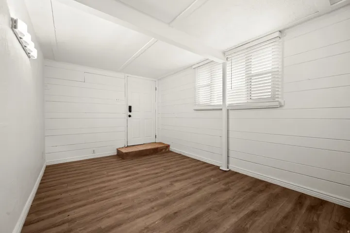 Wood-finish flooring, white shiplap walls, white door, and white window blinds