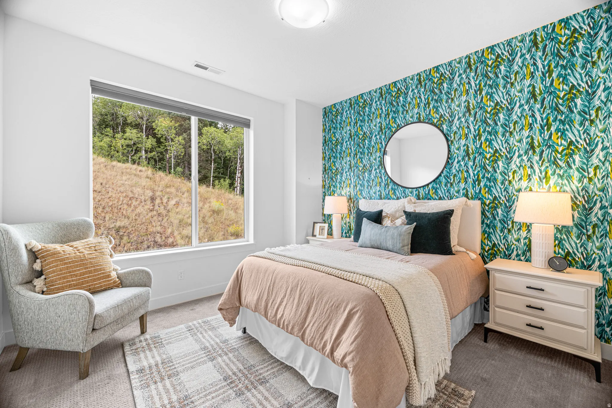 Large window with roller shade, accent wall with botanical pattern, wall-mounted circular mirror, and built-in ceiling light fixture