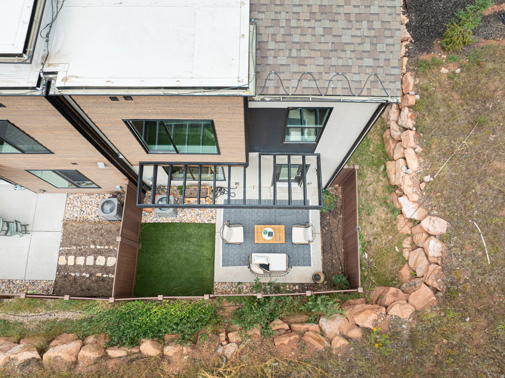 Rear exterior featuring a patio with a partial awning, an artificial turf area, and a rock retaining wall