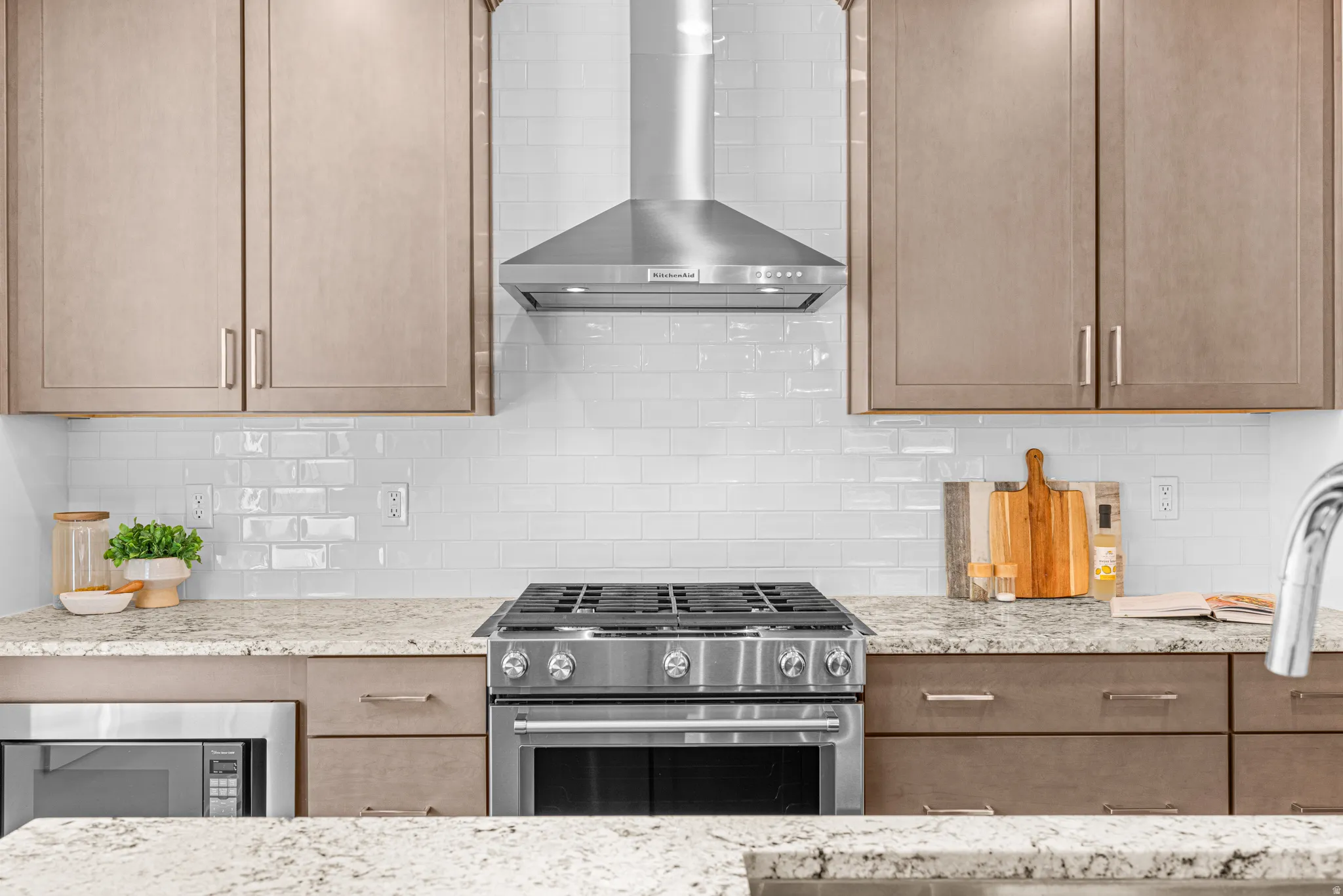 Stainless steel range with a coordinating range hood, white subway tile backsplash, light-toned cabinetry, and light speckled countertops