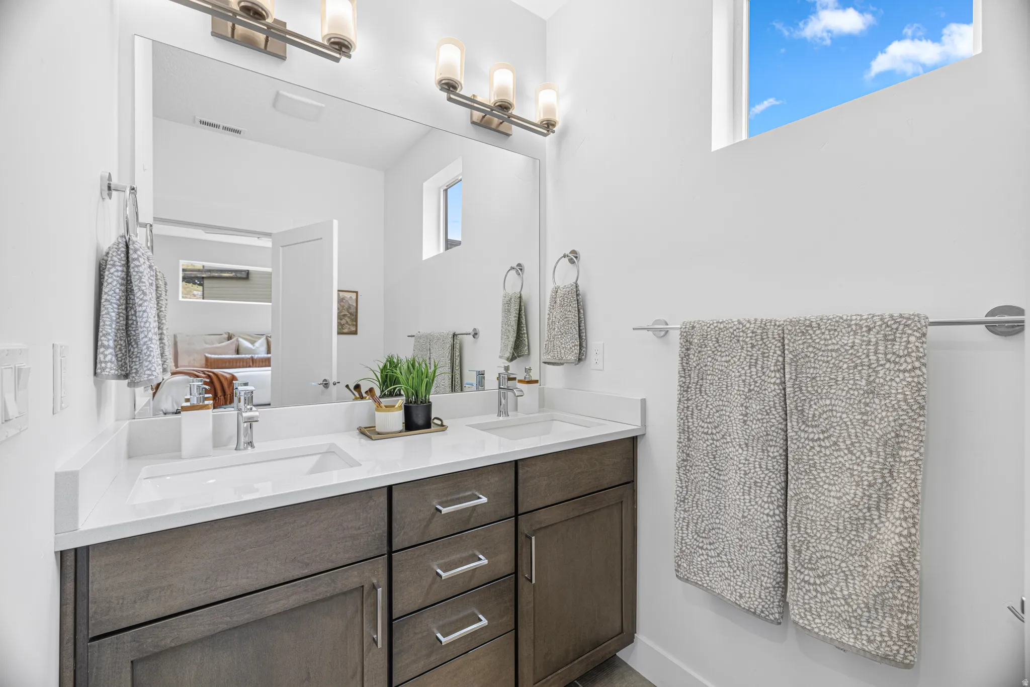 Dual vanity with undermount sinks and white countertops, complemented by a large mirror and brushed nickel light fixtures