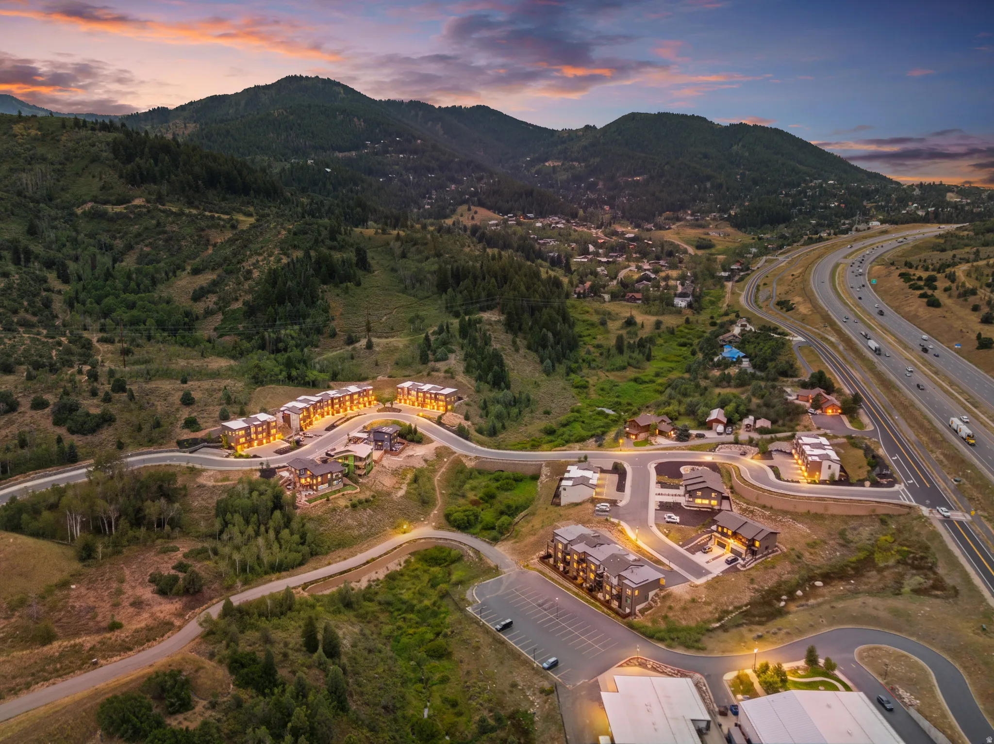 Aerial perspective featuring multiple residential structures, winding roadways, and surrounding natural terrain