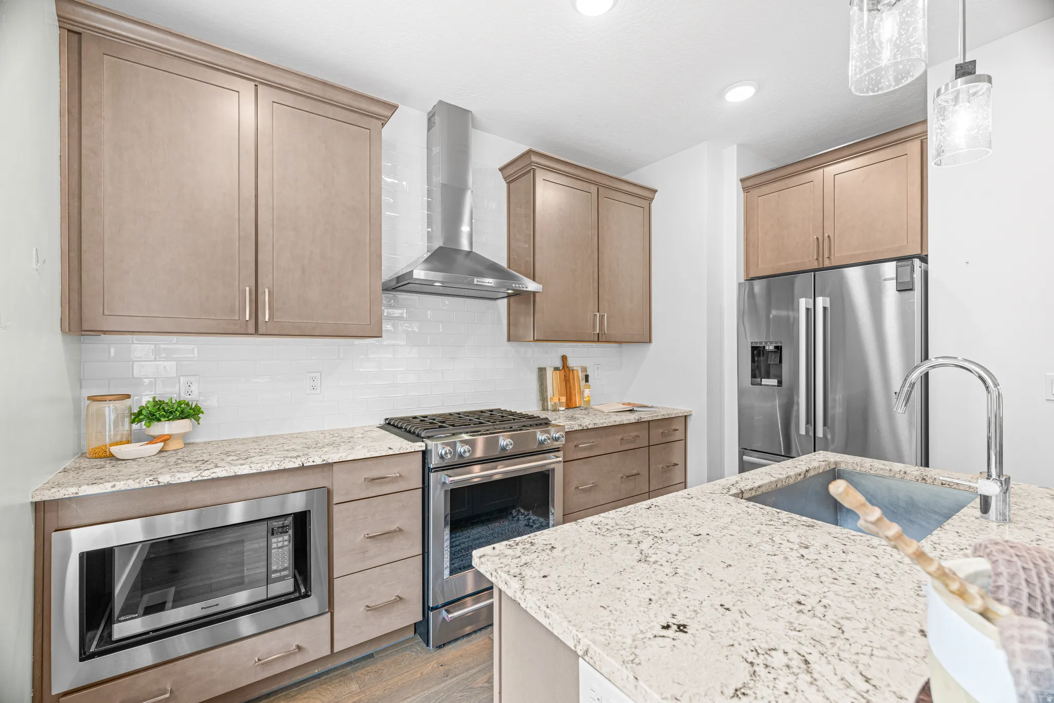 Stainless steel appliances, built-in microwave, light-toned cabinetry, subway tile backsplash, and light speckled countertops
