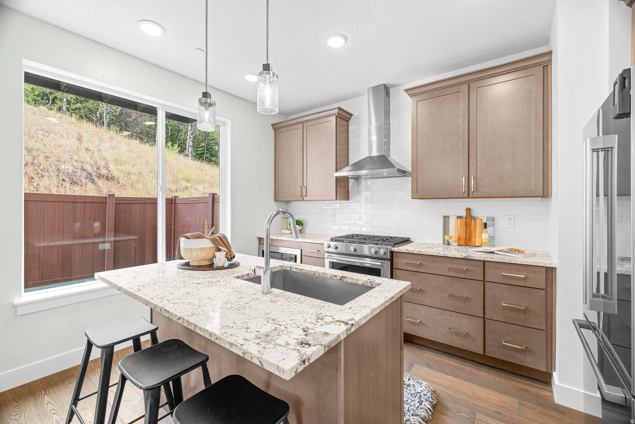 Kitchen with wood-finish flooring, an island featuring a drop-in sink and stone countertop, and pendant lighting