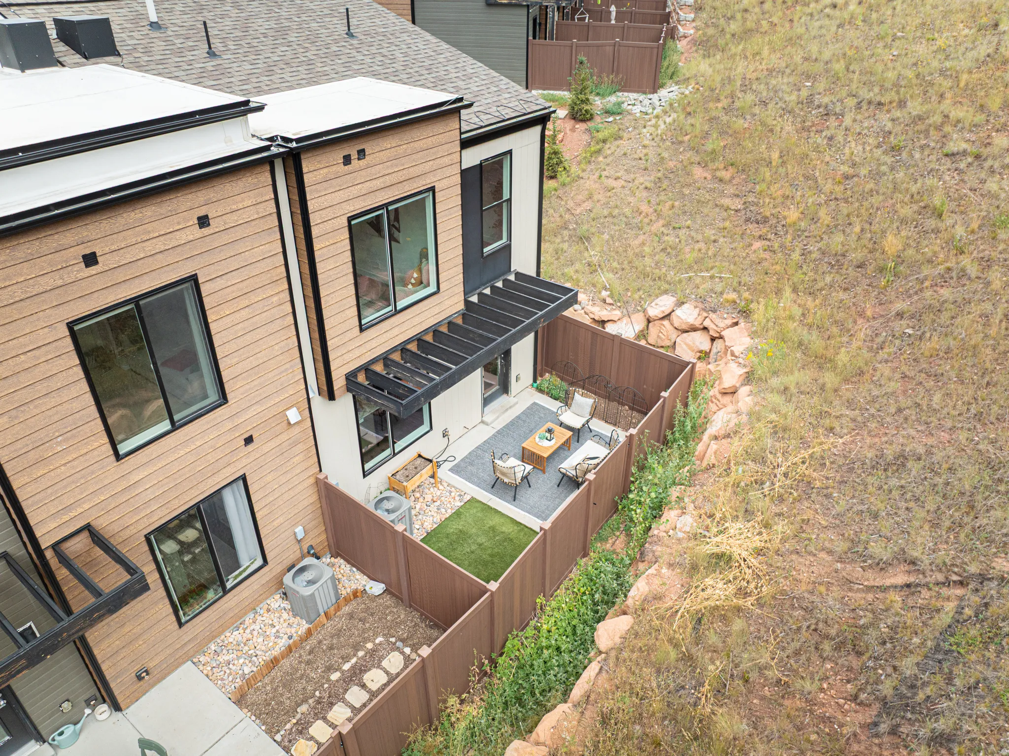 Private fenced patio with a pergola, artificial turf, and adjacent natural landscaping