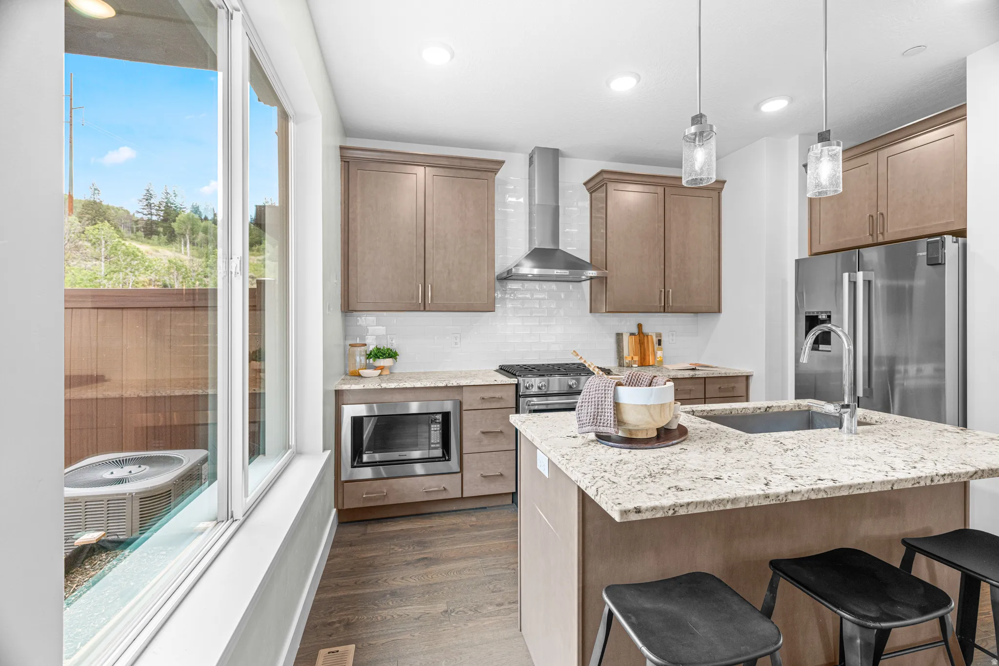 Open-concept kitchen featuring an island with a built-in sink, stainless steel appliances, contemporary pendant lighting, and wood-finish flooring