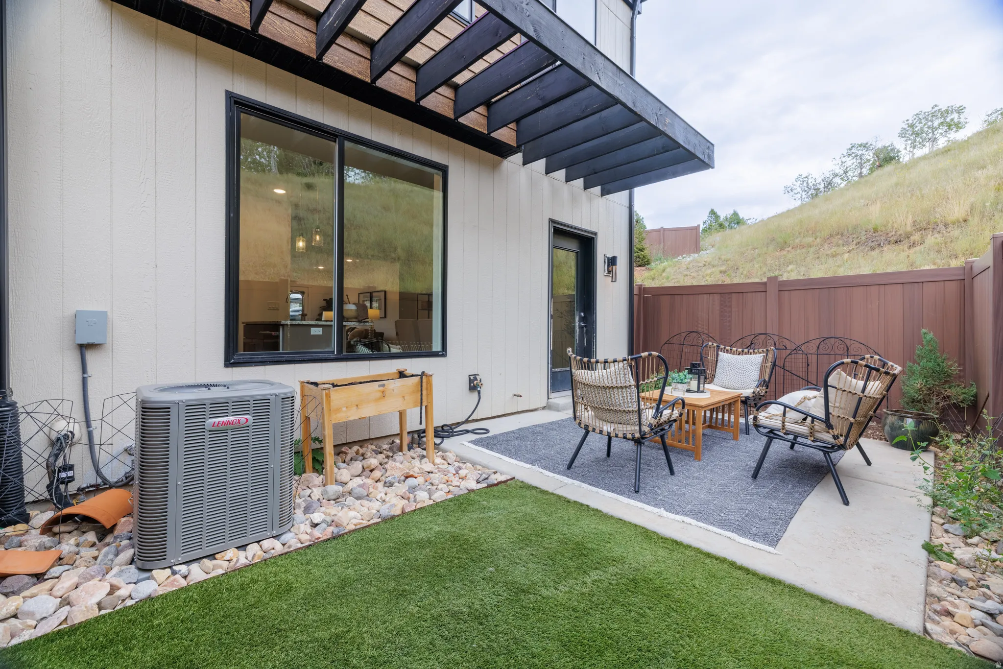 Concrete patio with a dark wood pergola, artificial turf, and a brown privacy fence