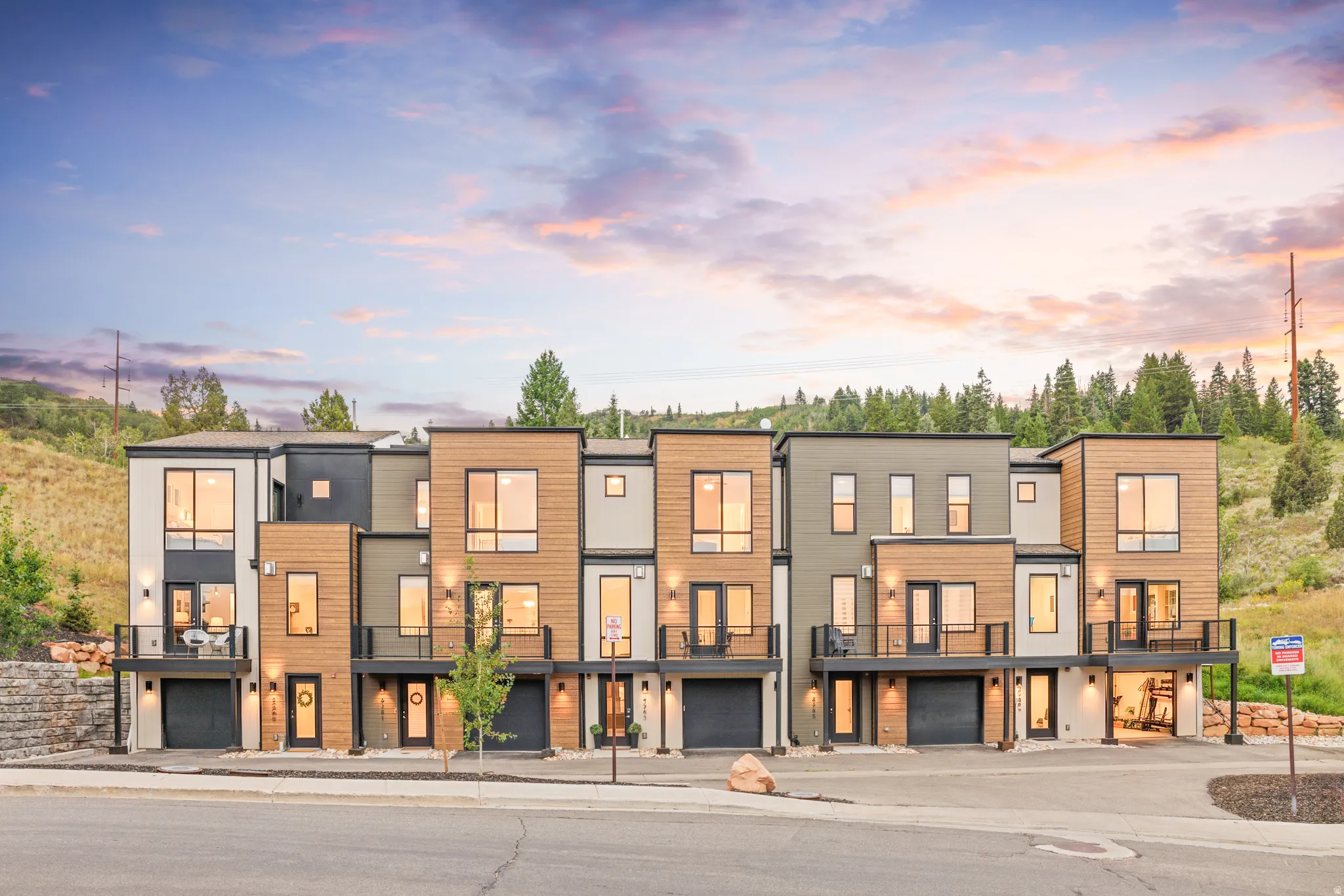 Modern townhome exteriors featuring wood-look siding, large windows, attached garages, and private balconies