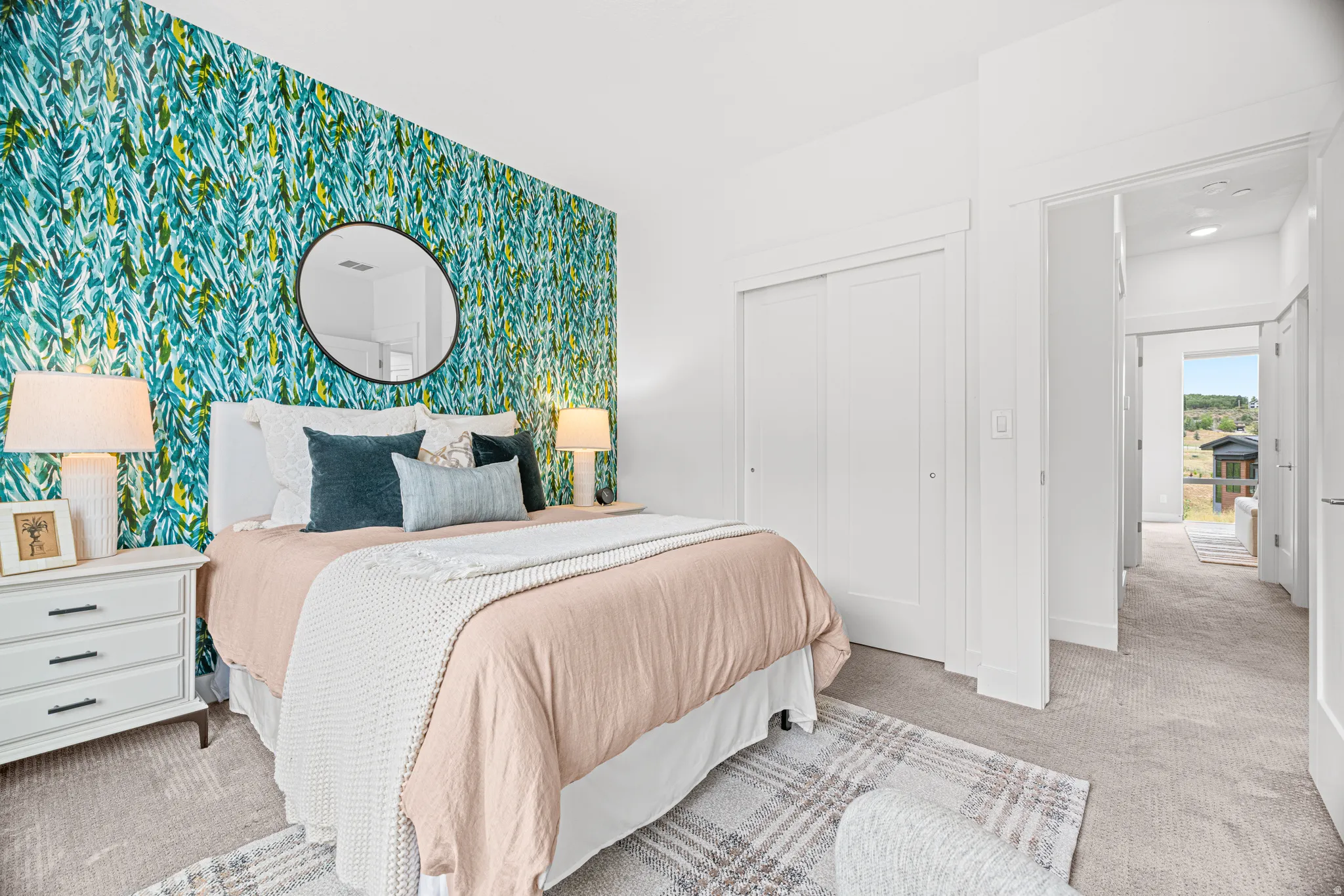 Primary Bedroom featuring a striking turquoise patterned accent wall, round mirror, bedside table with integrated drawers, table lamp with linen shade, and plush area rug
