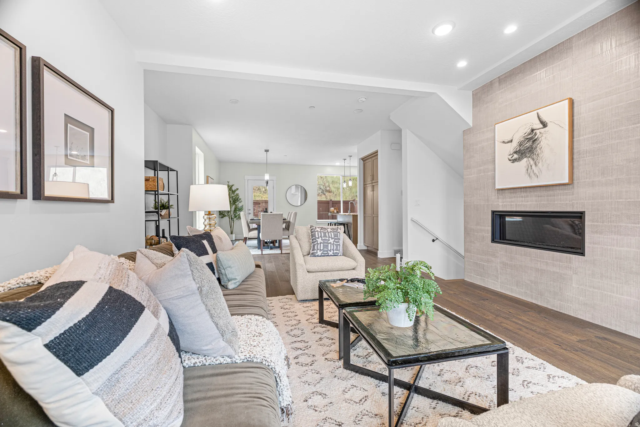 Recessed lighting illuminates the living area with wood-finish flooring and a tiled accent wall featuring a linear electric fireplace