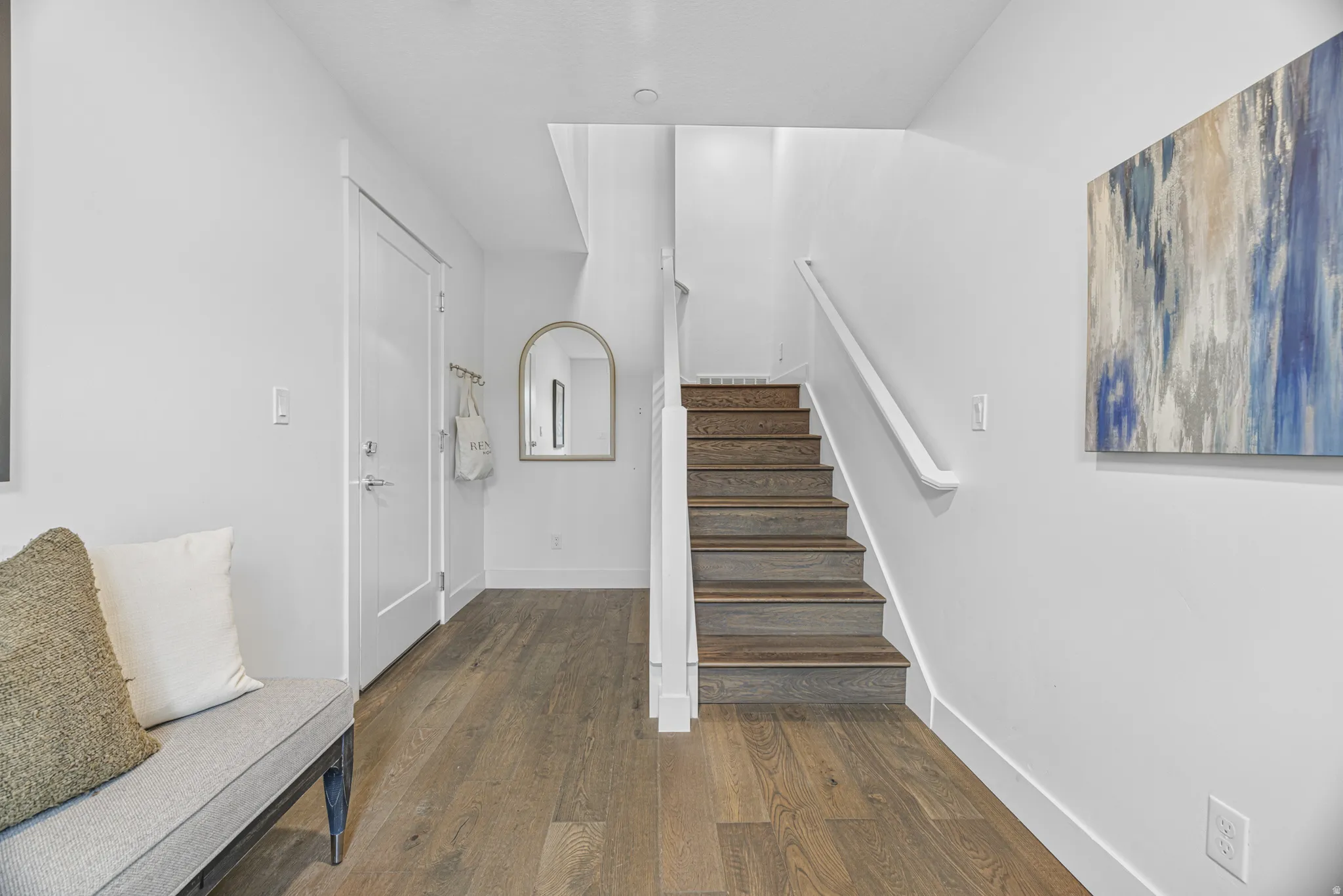 Wood-finish flooring throughout, white walls, staircase with wood-finish treads and white railing, and a white interior door