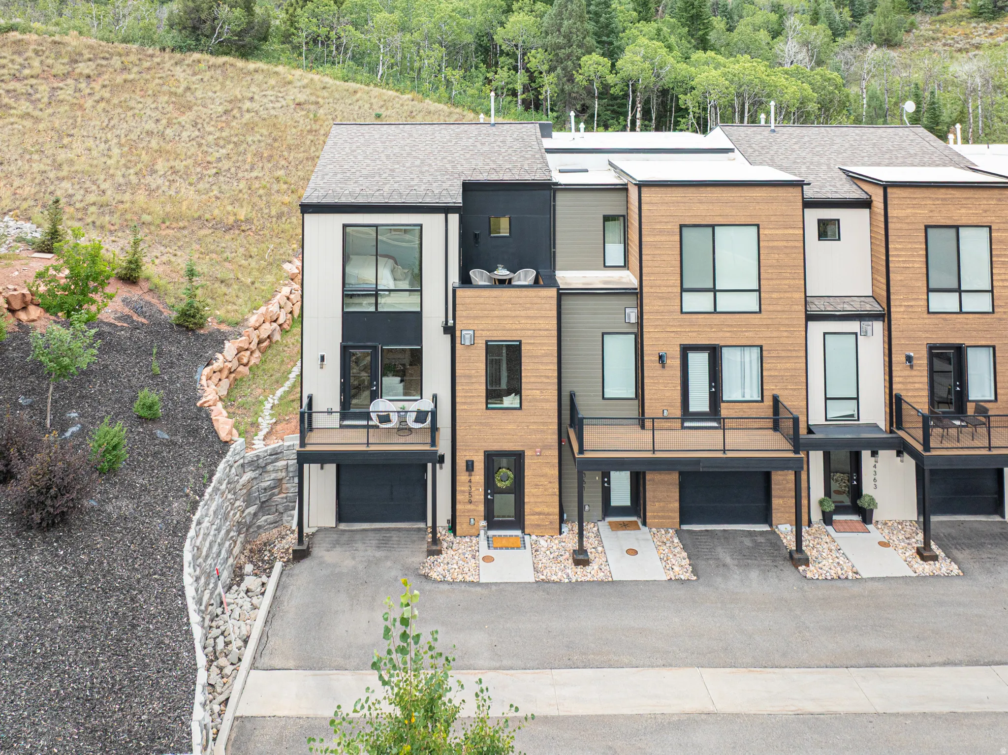 Modern townhome exterior featuring multi-level balconies, expansive windows, dark frame garage doors, and natural wood-tone siding accents