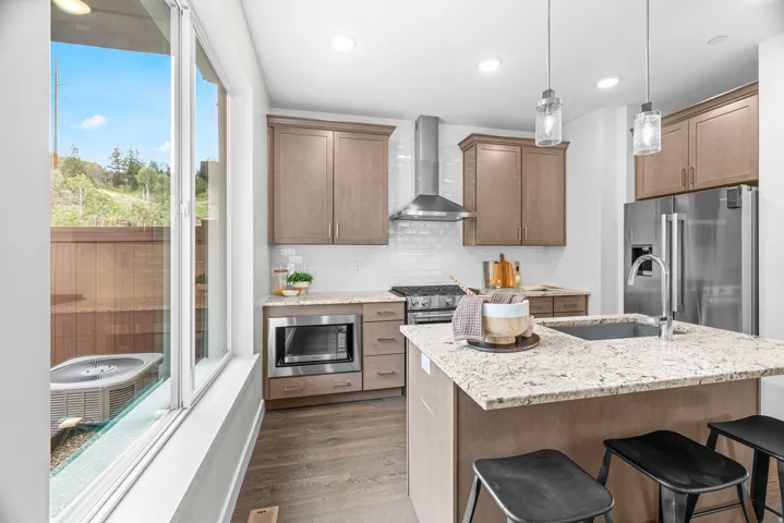 Open-concept kitchen featuring an island with a built-in sink, stainless steel appliances, contemporary pendant lighting, and wood-finish flooring