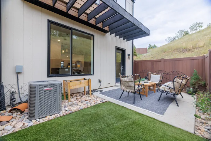 Concrete patio with a dark wood pergola, artificial turf, and a brown privacy fence