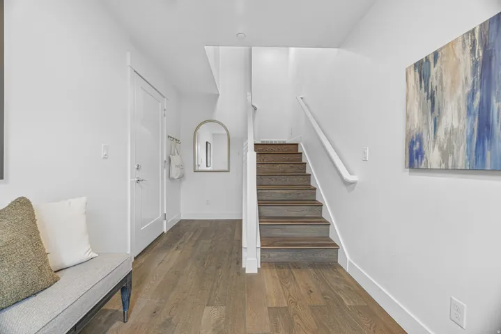 Wood-finish flooring throughout, white walls, staircase with wood-finish treads and white railing, and a white interior door