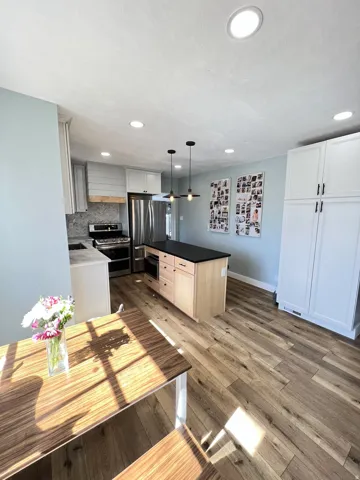 Kitchen featuring light wood-finish flooring, a central island with a dark countertop, white and light gray cabinetry, and recessed lighting