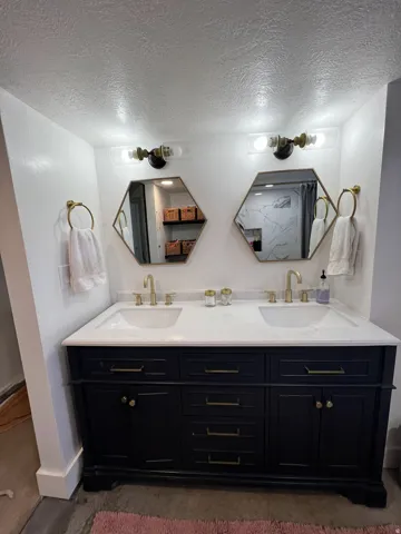 Dual vanity with a white countertop and integrated sinks, dark cabinetry with brass hardware, and two hexagonal mirrors