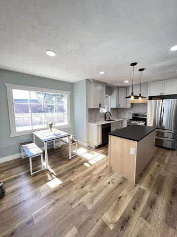 Kitchen featuring wood-finish flooring, white cabinetry, a kitchen island with a dark countertop, stainless steel appliances, and recessed lighting