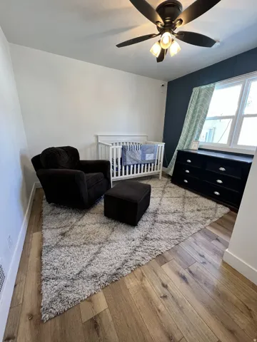 Wood-finish flooring, a ceiling fan with integrated lighting, and a window with white trim