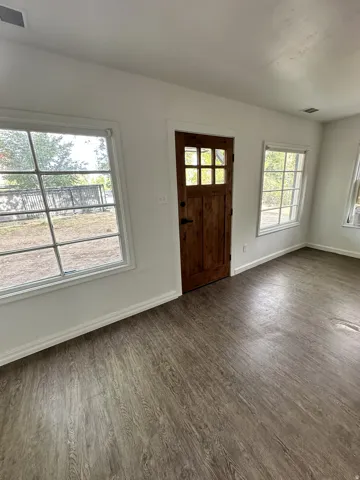Wood-finish flooring, white walls, multiple windows, and a wood entry door with glass panels