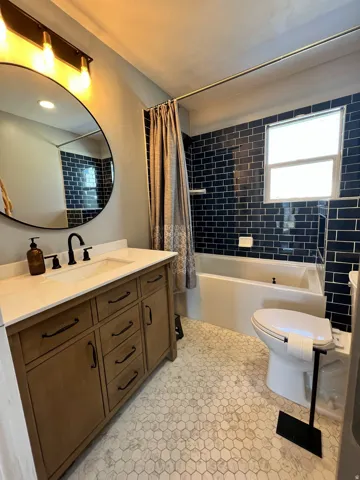 Bathroom featuring a wood-finish vanity with a white countertop, hexagonal floor tiling, a deep soaking tub, and subway tile accents