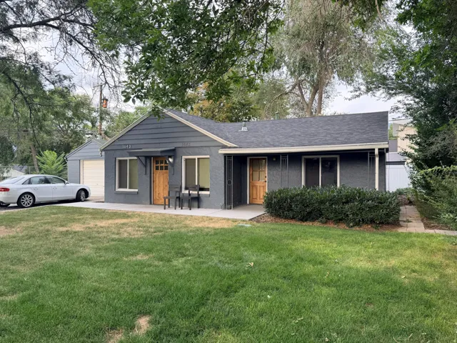 Front exterior featuring a dark gray facade, natural wood front door, covered entry, attached garage, and mature landscaping
