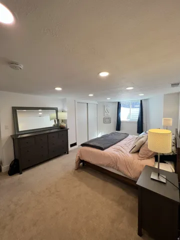 Plush carpeting, recessed lighting, white walls, and a window with dark drapery