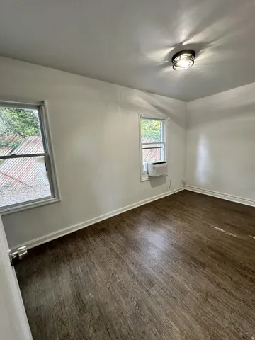 Room featuring wood-finish flooring, white panel walls, and two windows