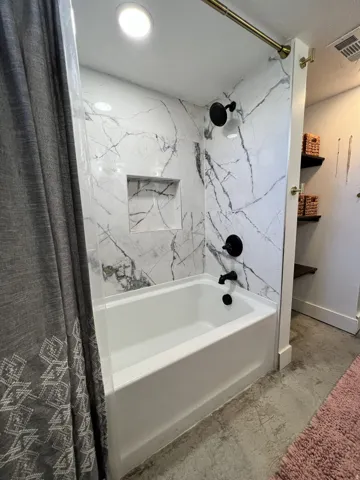 Bathtub with white marble-look surround, recessed niche, matte black fixtures, and recessed lighting