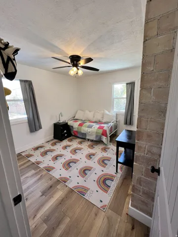 Bright secondary bedroom with ceiling fan and light fixture, wood-finish flooring, and large windows providing natural light