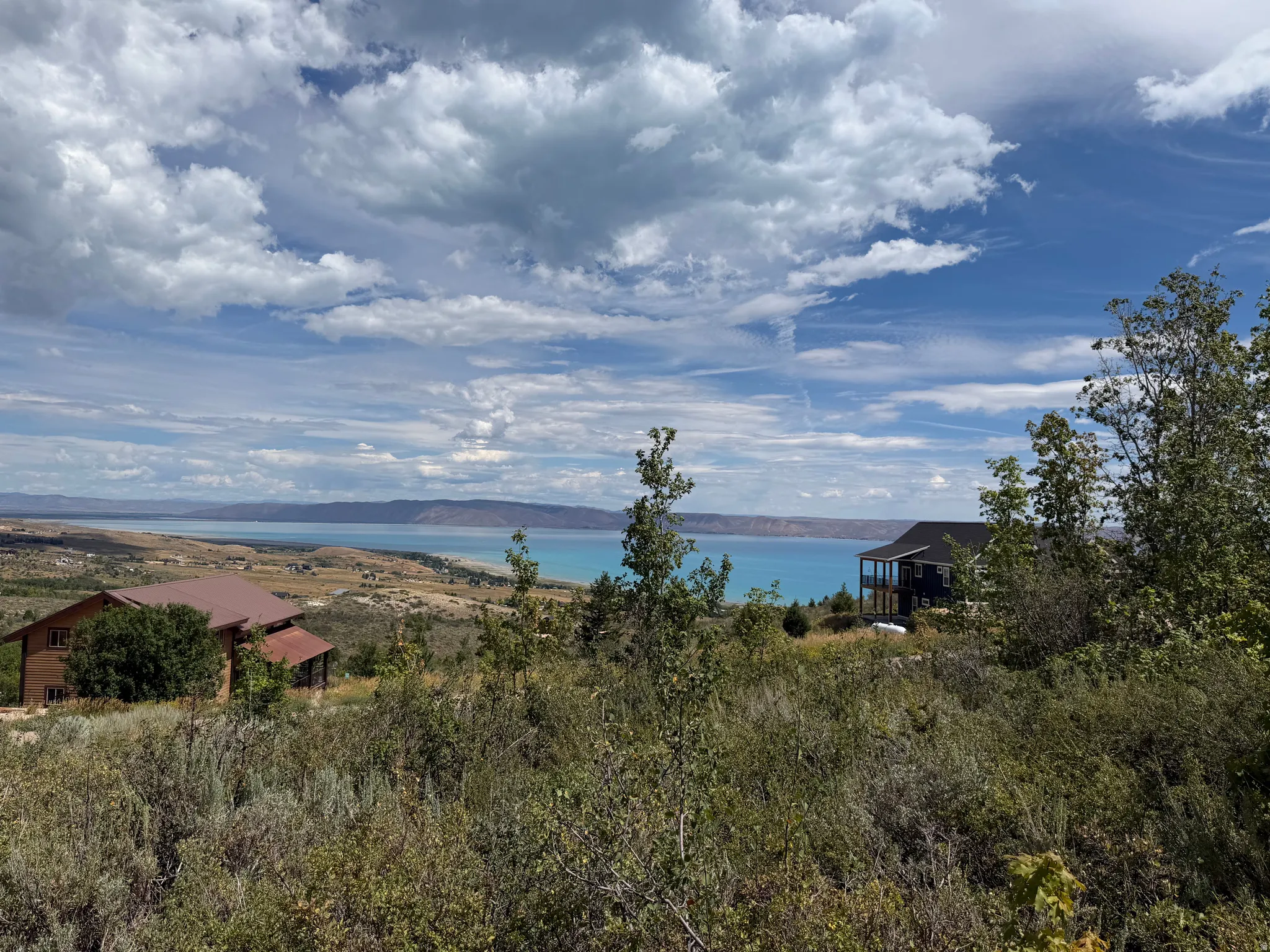Expansive landscape featuring distant water, mountainous terrain, and two distinct residential structures