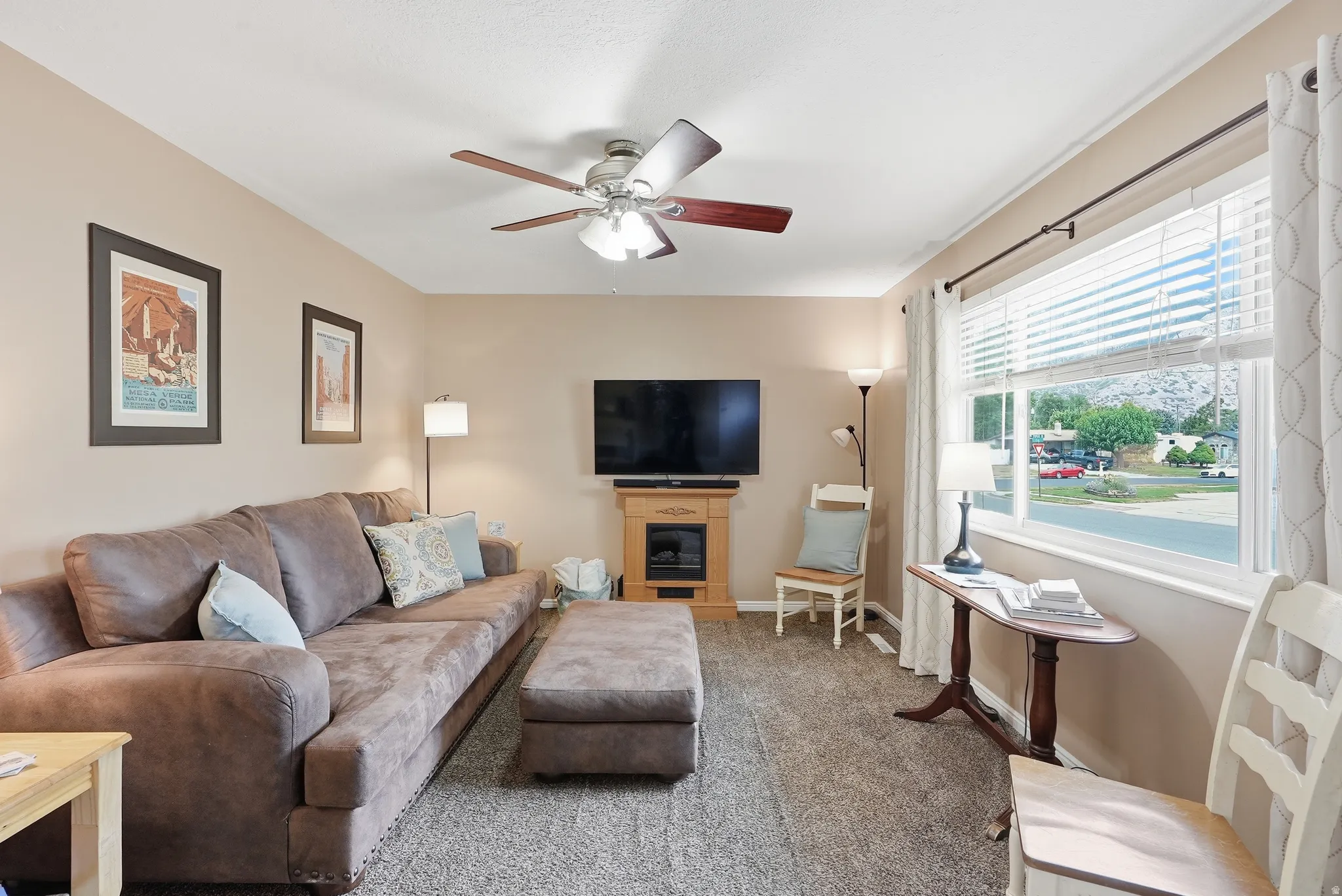 Carpeted living area with a ceiling fan, large window, and a built-in fireplace feature with a wood mantle