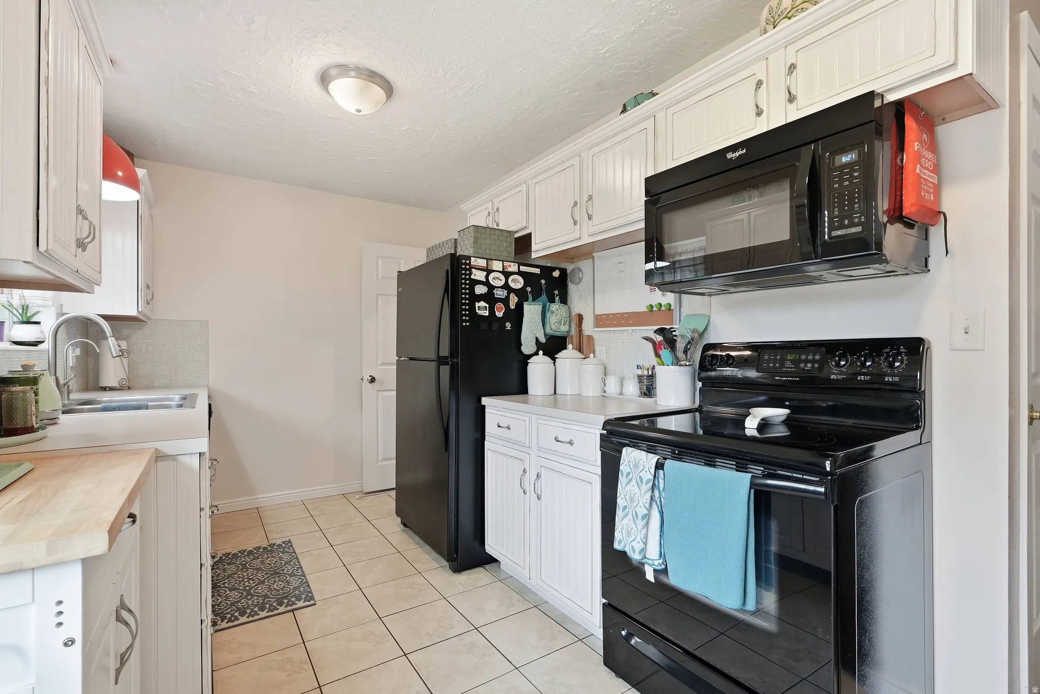 White cabinetry, black appliances, tile flooring, and laminate countertops