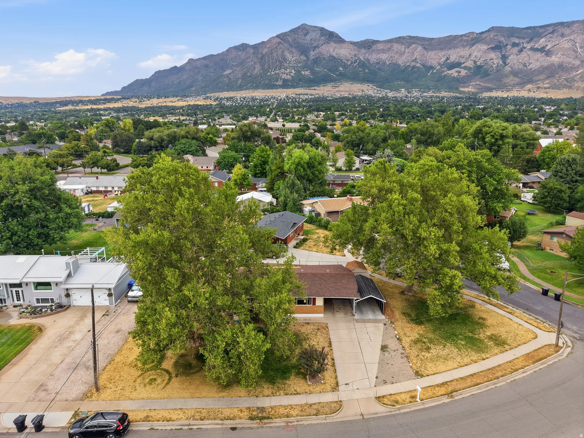 Mountain backdrop with extensive residential area, corner lot property, mature trees, and a concrete driveway with an attached carport