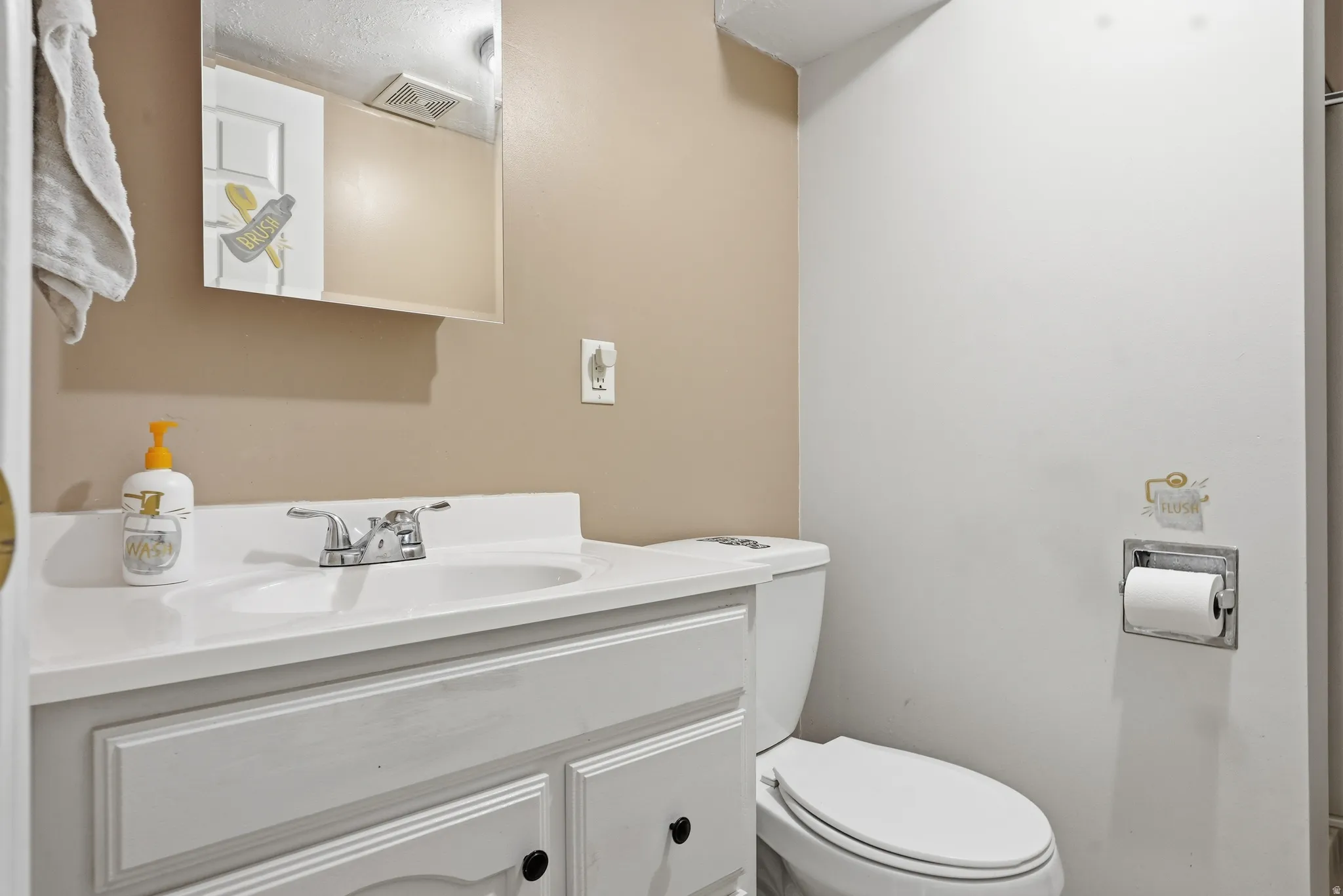 Vanity with integrated sink, chrome faucet, white cabinetry, wall-mounted mirror, and toilet