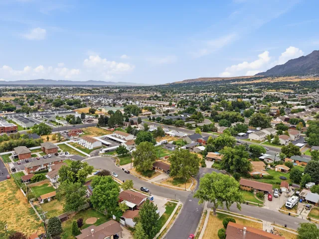 Neighborhood setting with established residential properties and mature trees, framed by distant mountains and a clear sky