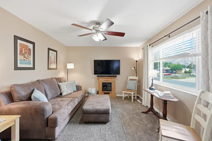 Carpeted living area with a ceiling fan, large window, and a built-in fireplace feature with a wood mantle