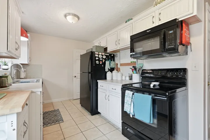 White cabinetry, black appliances, tile flooring, and laminate countertops