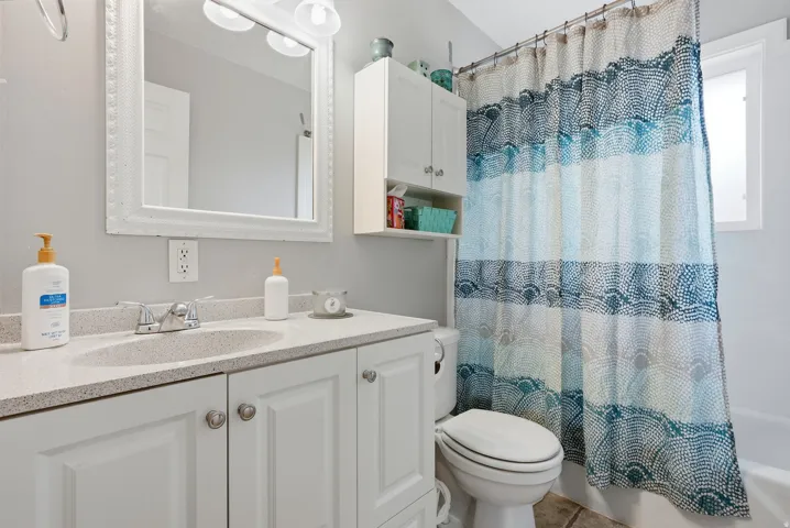 Bathroom featuring a single vanity with white cabinetry, a light-toned countertop, a framed mirror, and an overhead light fixture