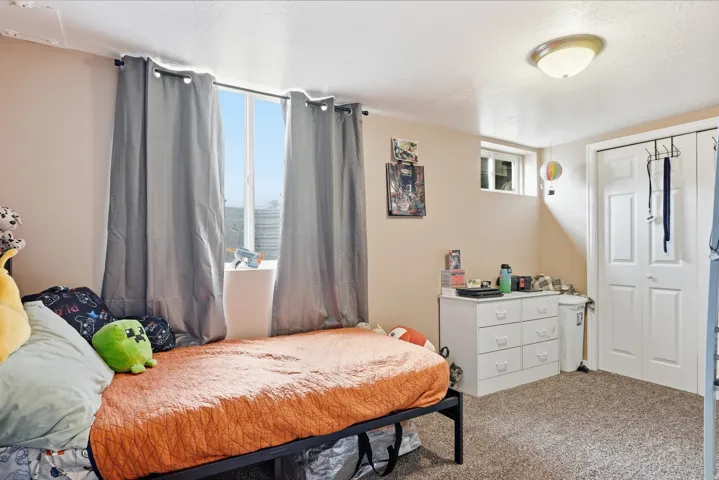Carpeted flooring, egress window, white bi-fold closet doors, and flush-mount ceiling light
