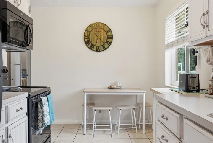 White cabinetry with decorative hardware, tile flooring, window with blinds, and white countertops