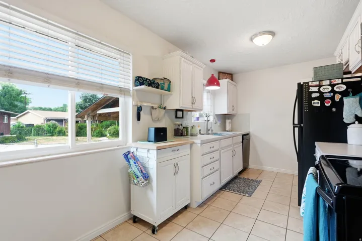White cabinetry, tile flooring, white sink, and window with blinds